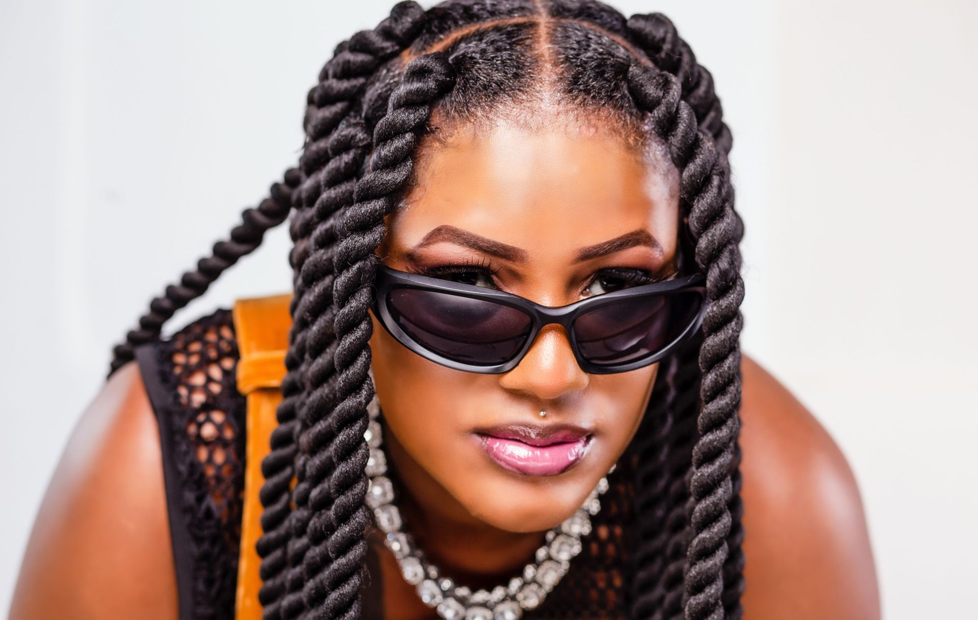 Close-up portrait of a fashionable woman with sunglasses and twisted hairstyles, exuding confidence.