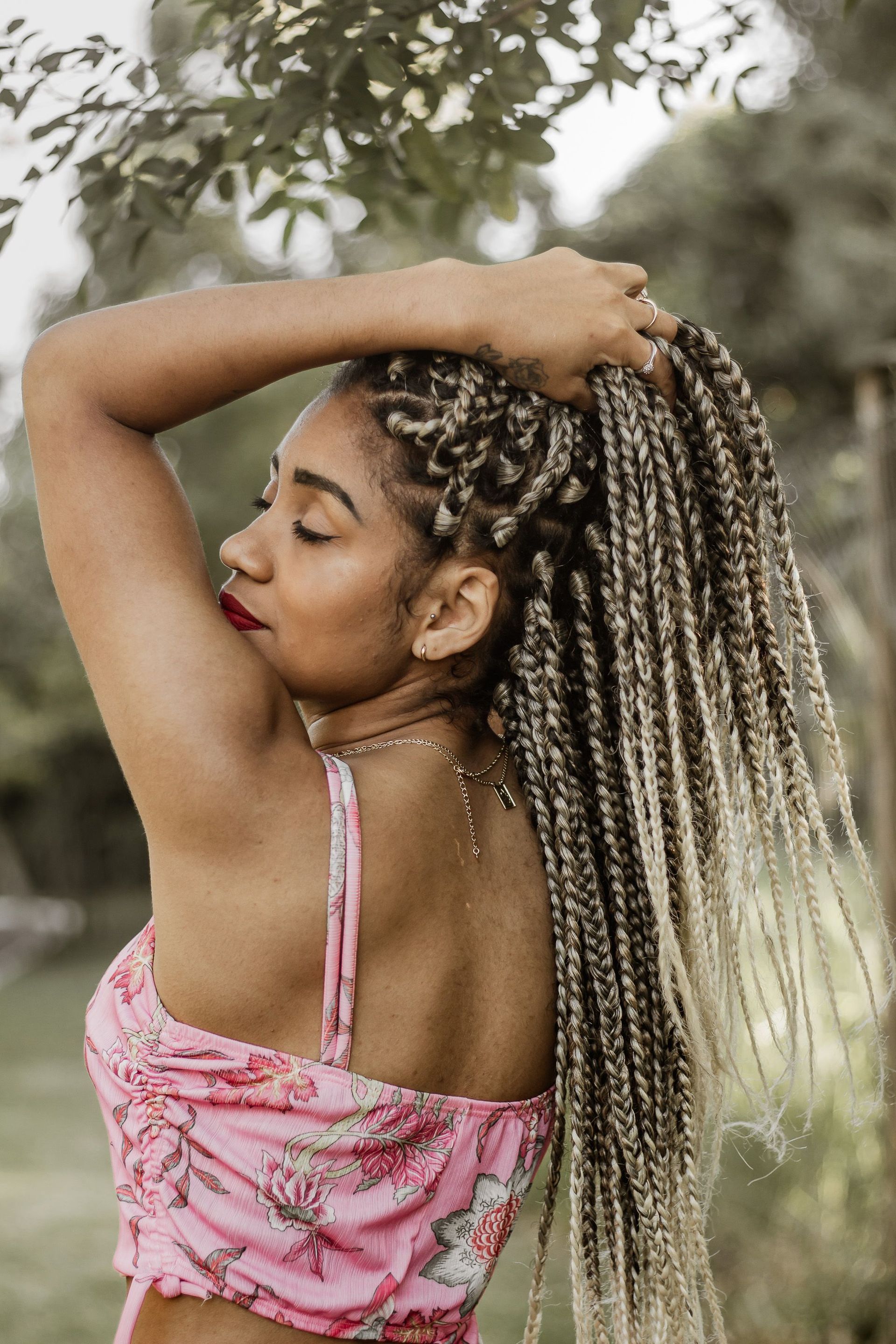 Woman with braided hair in a pink top enjoying outdoors, serene and stylish.