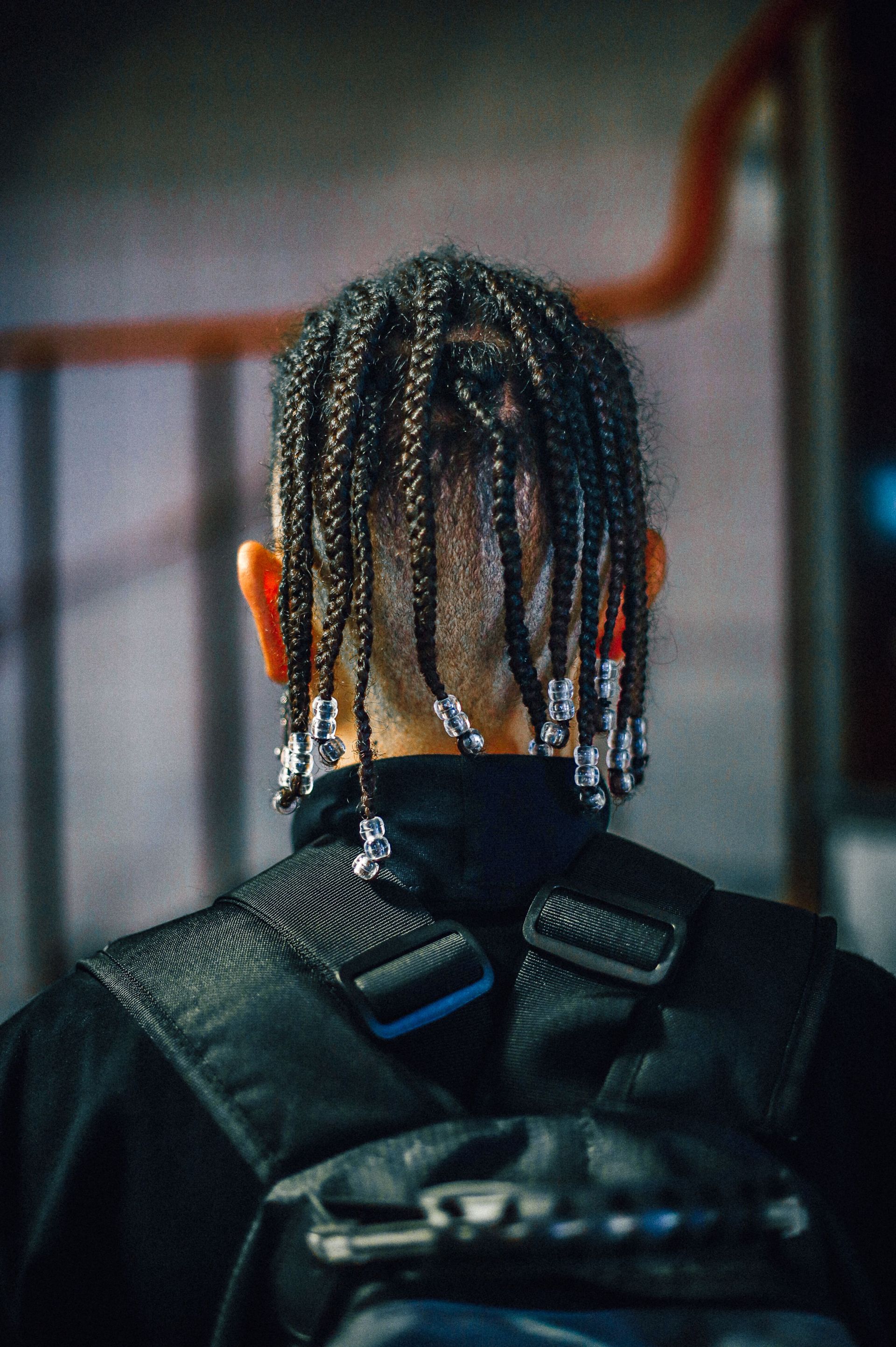 A person with braided hair wearing a backpack seen from behind indoors.