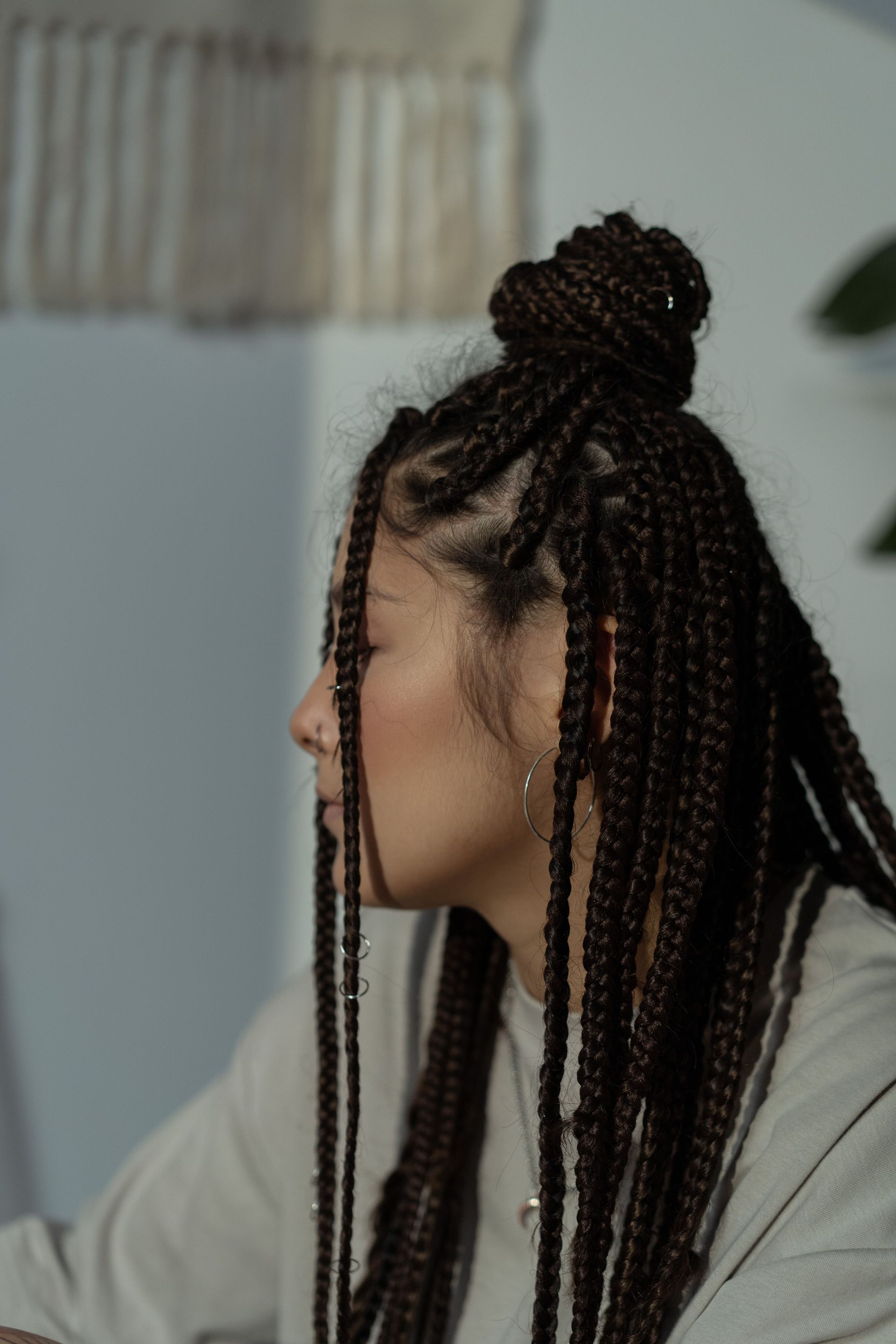 Side profile of woman with intricate afro braid hairstyle indoors, displaying modern fashion sense.