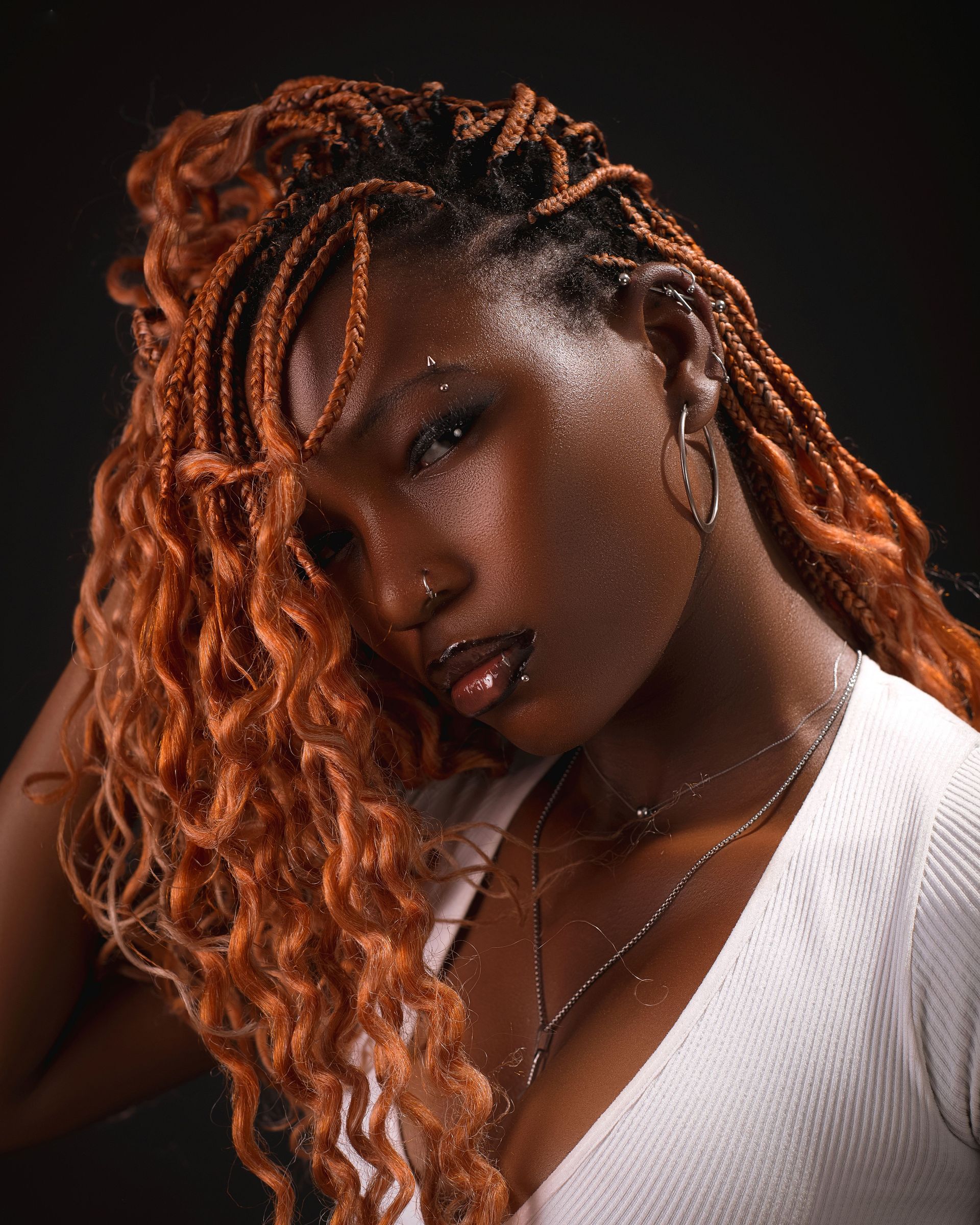 Elegant portrait of a woman with intricate braided hair and stylish accessories against a dark background.