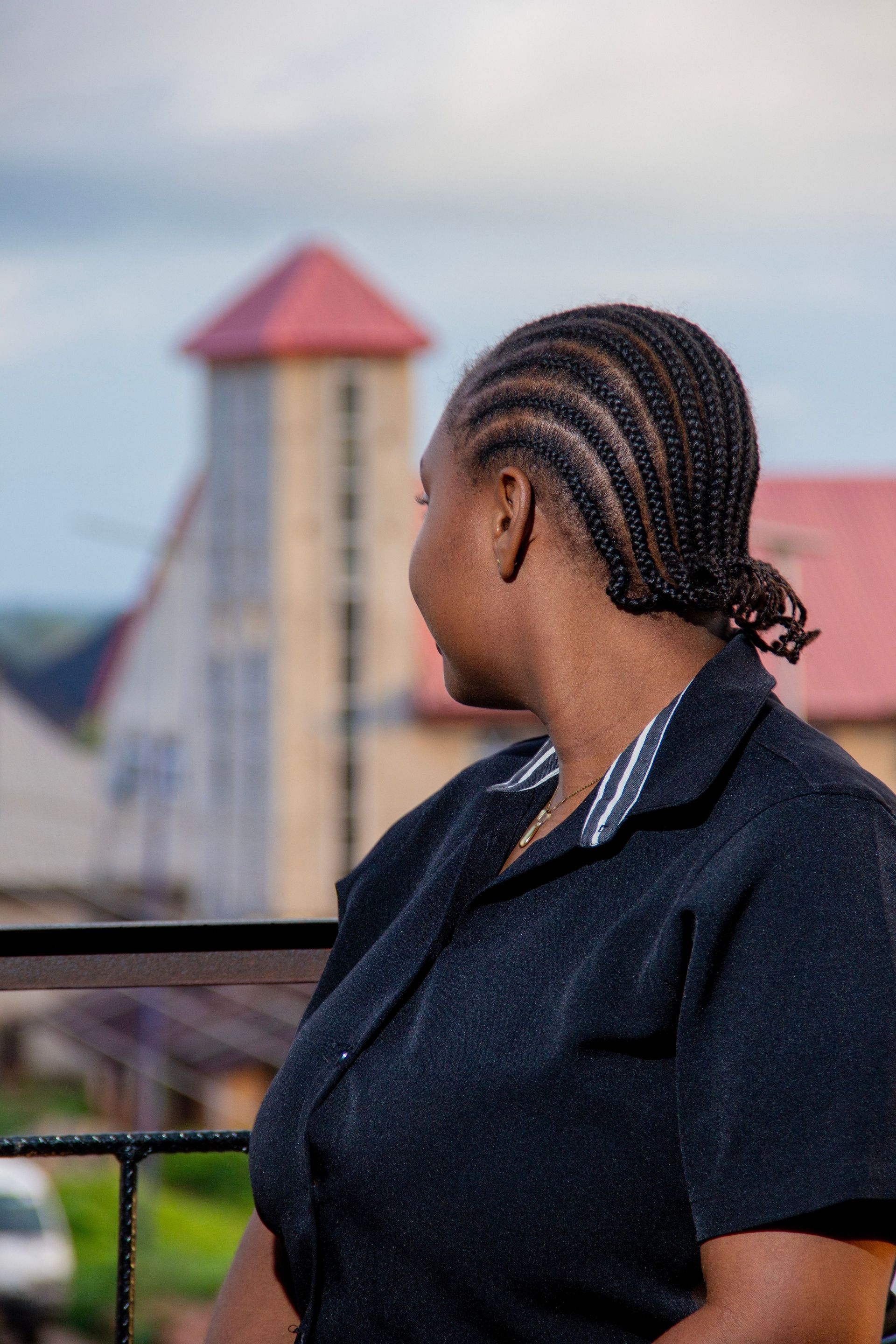 Woman with braided hair gazing at a building with red roofs, outdoors.