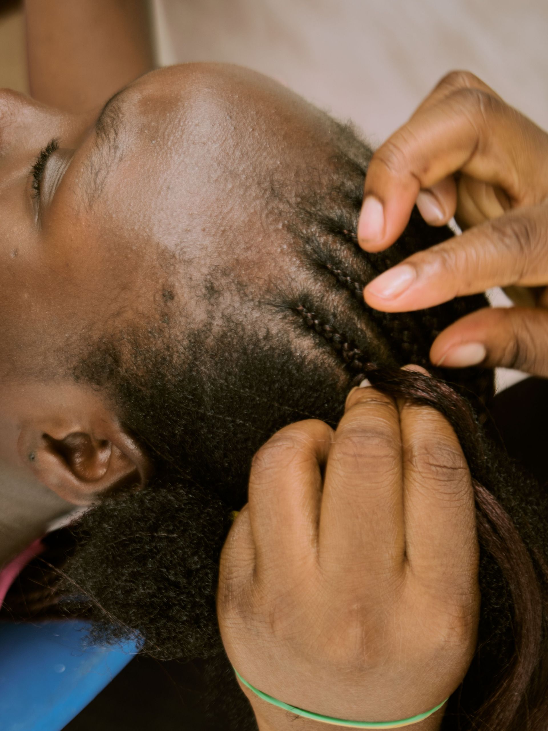 A detailed close-up shot of an African woman having her hair braided by skilled hands.